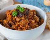 Pyszny bigos w białej misce, z gałązką natki pietruszki. Obok kromki chleba. Idealny na zimowe wieczory.
