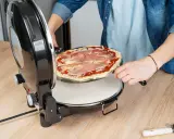 Osoba wkłada pizzę z szynką do okrągłego piekarnika. Idealny moment na pieczenie pizzy w piekarniku!