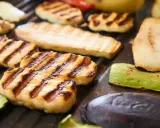 Grillowany ser halloumi z paskami od rusztu, obok cukinia, bakłażan i inne warzywa.