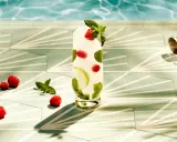 Orzeźwiający drink z malinami i miętą, idealny do Bacardi malinowego. Obok leżą maliny, a w tle widać basen i okulary przeciwsłoneczne.