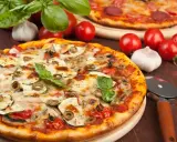Pizza z cukinią, oliwkami i pomidorkami, obok surowe pieczarki na pizze, czosnek i bazylia.