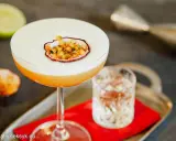 Pyszny drink Pornstar Martini z pianką i owocem marakui, obok kieliszek z drinkiem i połówka limonki.
