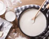 Gładki sos beszamelowy w patelni, obok mleko, masło i gałka muszkatołowa. Idealny do zapiekanek.