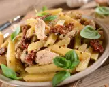 Penne z kurczakiem i suszonymi pomidorami, udekorowane świeżą bazylią. Pyszne danie na obiad.