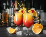 Dwa drinki z wódką, ozdobione pomarańczą i wiśnią, na tle barowych butelek. Idealne na letnie wieczory.