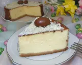 Pyszny sernik z mascarpone, udekorowany czekoladowymi jajeczkami i wiórkami białej czekolady, na tle wielkanocnych ozdób.