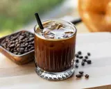 Orzeźwiający cold brew z lodem i słomką, obok miseczka z ziarnami kawy. Idealny na gorący dzień.
