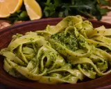Pappardelle z aromatycznym makaronem z pesto, podane na glinianym talerzu. W tle cytryny i rukola.