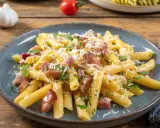 Penne rigate z chrupiącym boczkiem, posypane parmezanem i natką pietruszki. Pyszne makaron z boczkiem na talerzu.