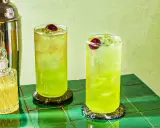 Dwa orzeźwiające drinki Tokyo Ice Tea z wiśniami i lodem, obok shakera i buteleczki z likierem.