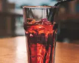 Szklanka z lodem i ciemnym napojem, idealne proporcje whisky z colą. Czarna słomka zanurzona w napoju.