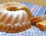 Puszysta babka wielkanocna, oprószona cukrem pudrem, leży na niebiesko-białym ręczniku. Obok niej kilka kromek ciasta.