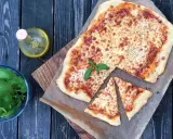 Pyszna pizza margherita z roztopionym serem i świeżą bazylią, obok butelka oliwy i miseczka ziół.