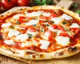 Pyszne ciasto na pizzę bez wyrastania, z pomidorami i mozzarellą, na drewnianej desce.