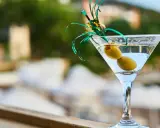 Orzeźwiający martini fiero drink z oliwkami, ozdobiony zieloną wstążką, na tle rozmytego, letniego krajobrazu.