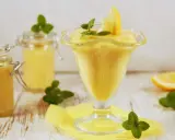 Aksamitny lemon curd w pucharku, ozdobiony plasterkiem cytryny i miętą. Obok słoiczki z tym samym kremowym przysmakiem.