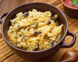 Pyszne risotto z warzywami, pełne grzybów i marchewki, podane w brązowej miseczce.