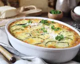Pyszna zapiekanka z cukinii, udekorowana natką pietruszki i startym parmezanem, prezentuje się apetycznie w białej naczyniu.