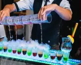 Barman nalewa kolorowe shoty z wielopoziomowego shakera. Efektowny drink bar diy z dymem i neonowym oświetleniem.