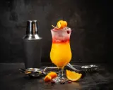 Kolorowy drink Sex on the Beach z pomarańczą i żurawiną, obok shakera i akcesoriów barmańskich. Idealny przepis na lato!