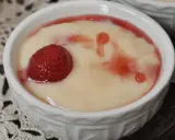Aksamitna masa budyniowa z truskawką i malinowym sosem w białej miseczce.