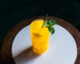 Orzeźwiający drink z mango, z kostkami lodu i listkiem mięty, podany w szklance ze słomką.
