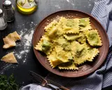 Pyszne ravioli z ricottą i szpinakiem, posypane parmezanem, na brązowym talerzu. Obok kawałki sera i przyprawy.