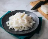 Gotowy do przygotowania makaron ryżowy na talerzu. Obok deska z nożem i stos świeżego makaronu.