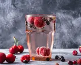 Orzeźwiający drink z wódką malinową, pełen malin, wiśni i borówek, bąbelkuje w szklance.