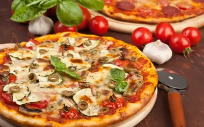 Pizza z cukinią, oliwkami i pomidorkami, obok surowe pieczarki na pizze, czosnek i bazylia.