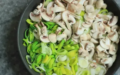 Na patelni pokrojone pieczarki i por, składniki na pyszny sos pieczarkowy przepis.