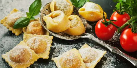 Świeże ravioli i tortellini, posypane cukrem pudrem, z pomidorkami koktajlowymi i bazylią. Idealne z czym podawać ravioli? Z prostym sosem!