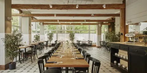 Elegancka sala restauracyjna z długimi stołami, idealna na degustację **primitivo kuchnia i wino**. Drewniane belki i duże okna tworzą przytulną atmosferę.