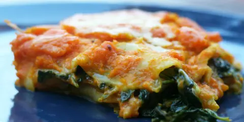Pyszne lasagne ze szpinakiem, z pomarańczowym sosem i ciągnącym się serem, na granatowym talerzu.