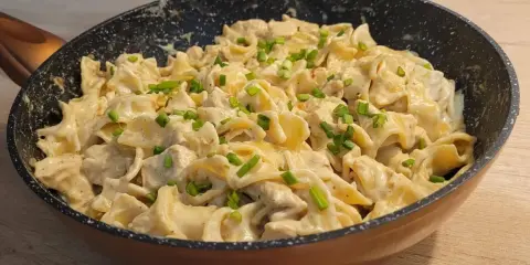 Tagliatelle z kurczakiem w sosie śmietanowym, posypane szczypiorkiem, podane w patelni. Pyszne danie gotowe do spożycia.