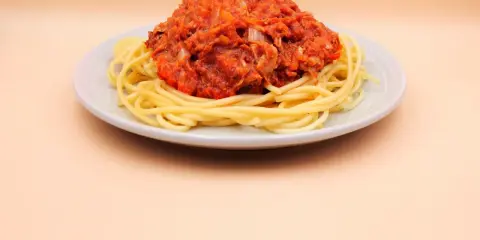 Porcja spaghetti z sosem pomidorowym i tuńczykiem, podana na jasnym talerzu.