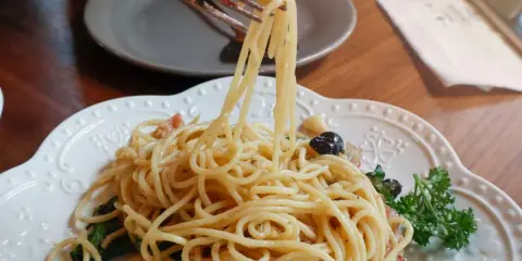 Widok z bliska na talerz pysznego spaghetti aglio e olio, z widelcem unoszącym porcję makaronu, pomidorkiem i bazylią.