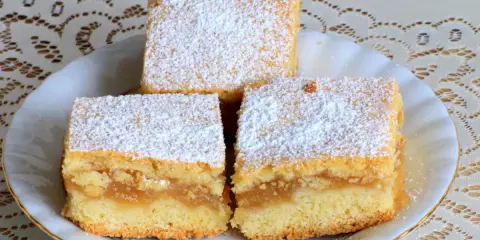 Pyszne ciasto z jabłkami, posypane cukrem pudrem, prezentuje się apetycznie na białym talerzyku.