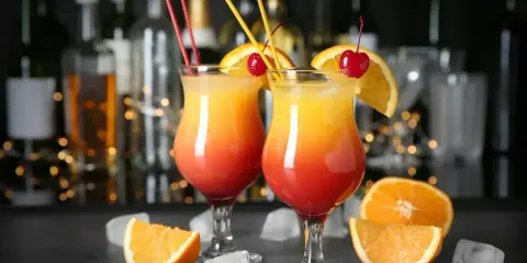 Dwa drinki z wódką, ozdobione pomarańczą i wiśnią, na tle barowych butelek. Idealne na letnie wieczory.