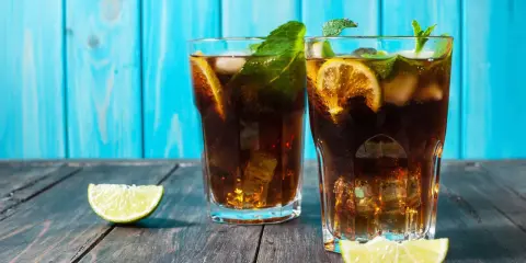 Dwa orzeźwiające drinki z rumem ciemnym, lodem, cytryną i miętą na drewnianym blacie.