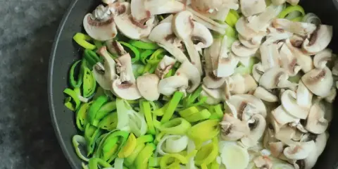 Na patelni pokrojone pieczarki i por, składniki na pyszny sos pieczarkowy przepis.