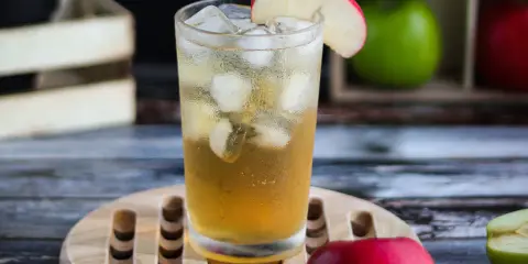 Orzeźwiający drink z sokiem jabłkowym, lodem i plasterkiem jabłka. W tle skrzynka z jabłkami.