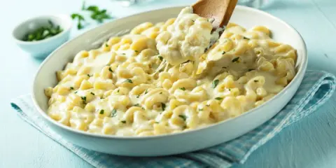 Pyszne mac and cheese przepis w białej misce, z drewnianą łyżką nabierającą porcję kremowego makaronu z serem.