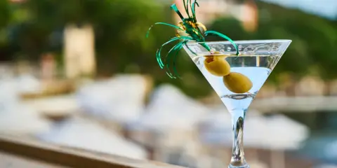 Orzeźwiający martini fiero drink z oliwkami, ozdobiony zieloną wstążką, na tle rozmytego, letniego krajobrazu.