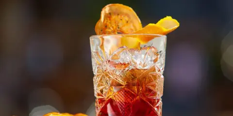 Klasyczny whisky old fashioned w kryształowej szklance, ozdobiony skórką pomarańczy i suszonym owocem.