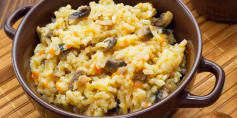Pyszne risotto z warzywami, pełne grzybów i marchewki, podane w brązowej miseczce.