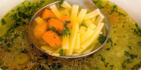 Łyżka nabiera aromatyczny bulion warzywny z marchewką i makaronem nitki.