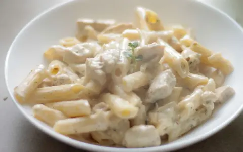 Penne z kurczakiem w kremowym sosie, udekorowane gałązką ziół. Pyszne danie, które zachwyci każdego smakosza.