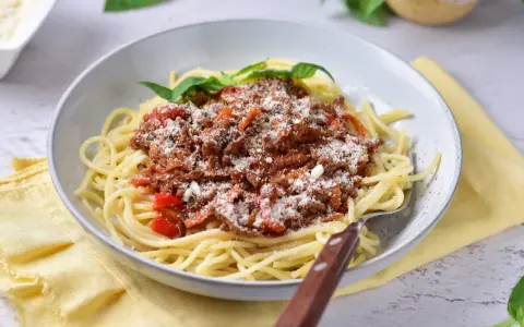 Pyszne spaghetti z bogatym sosem mięsnym na bazie passaty, posypane parmezanem i udekorowane listkami bazylii.