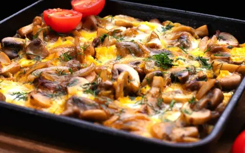 Zapiekane pieczarki z cebulą i serem, ozdobione pomidorkami koktajlowymi i koperkiem. Pyszne danie gotowe do podania.
